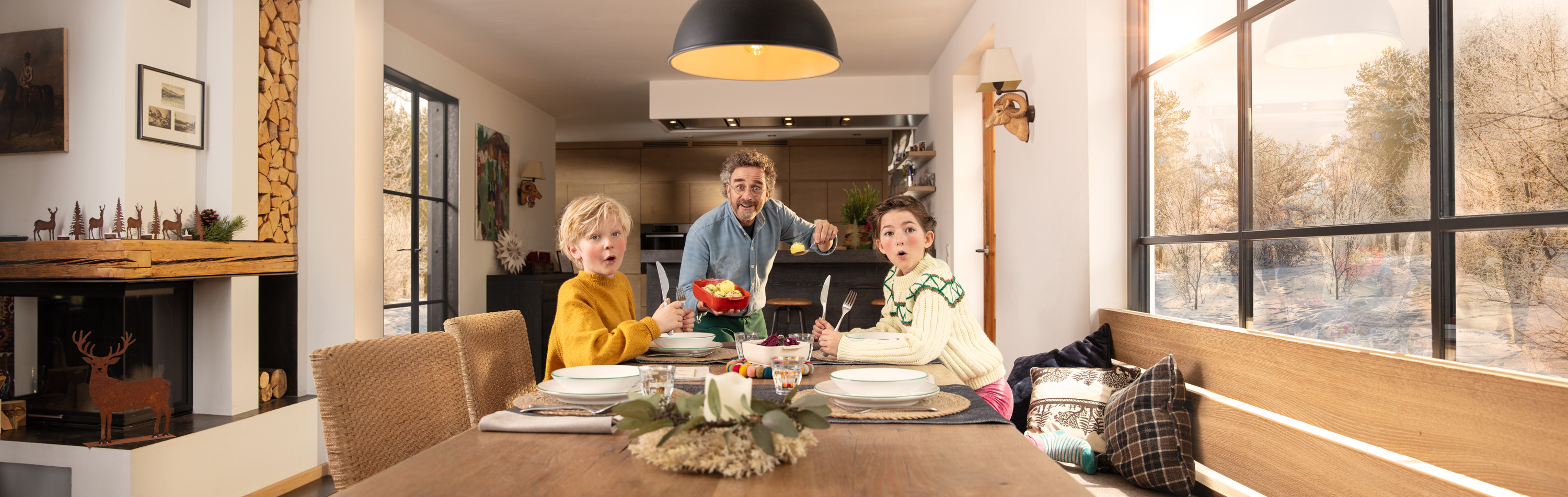 Ein Vater und seine Kinder sind gemeinsam am Esstisch und schauen überrascht in die Kamera.