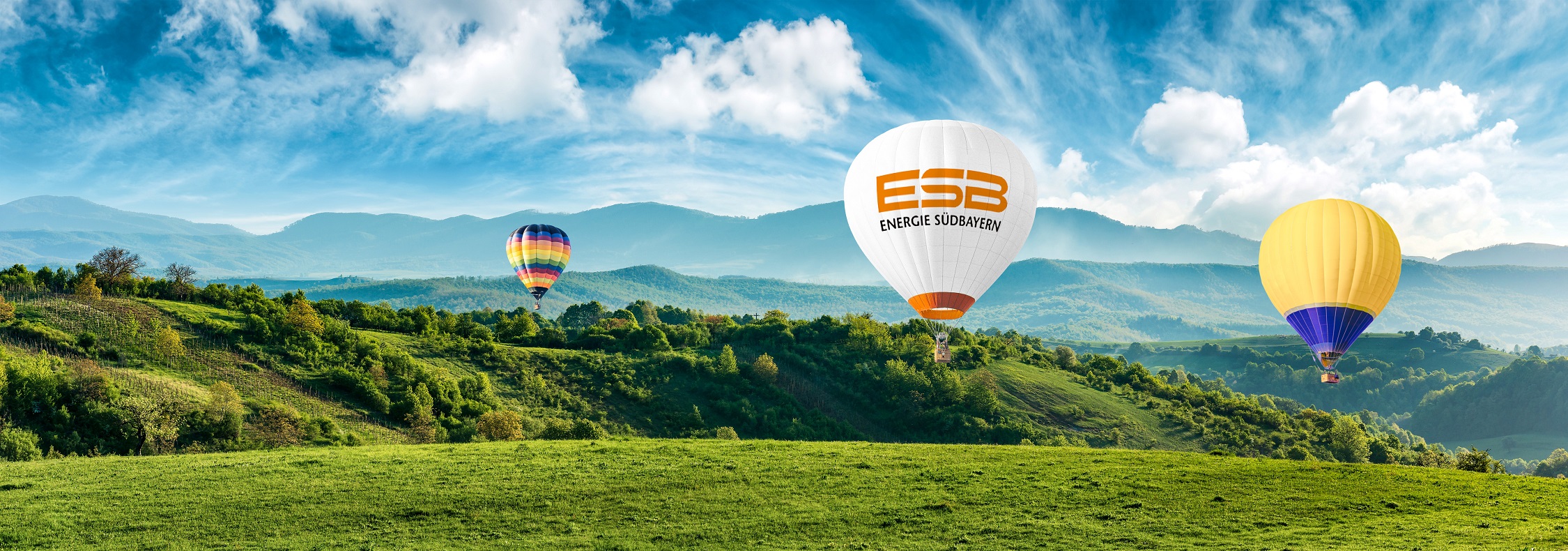 Drei Heißluftballone fahren durch eine Berglandschaft.