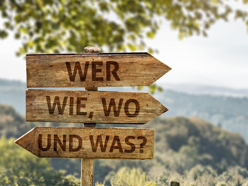 Holzschilder, auf denen die Frageworte: wer, wie, wo und was stehen.