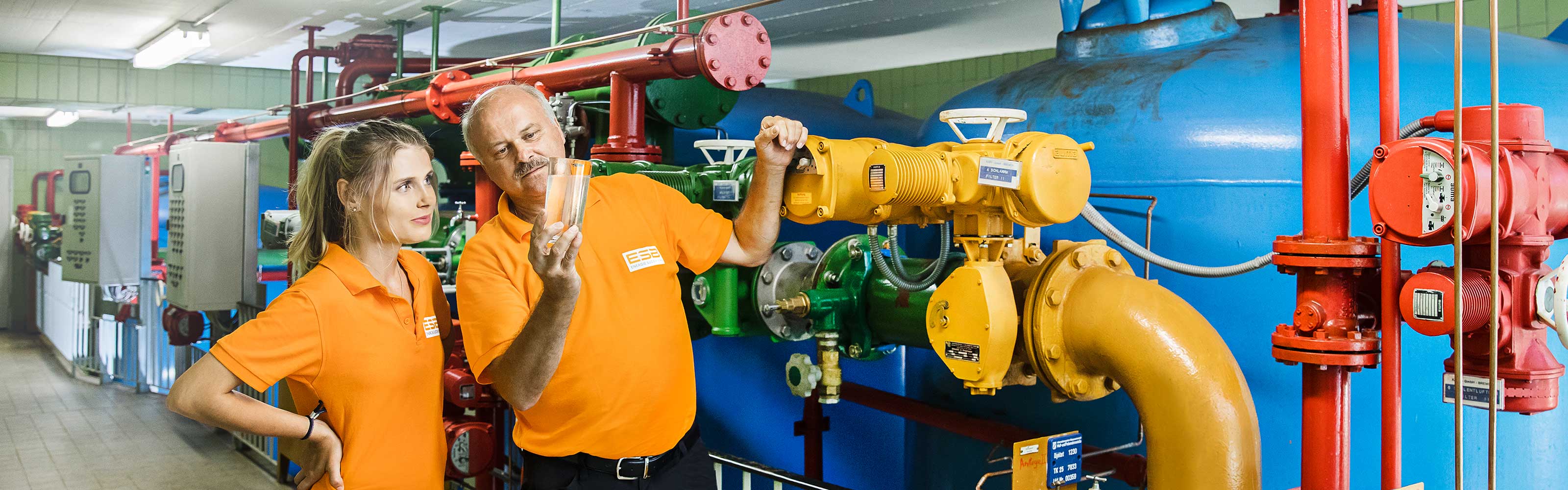 Eine Frau und ein Mann stehen in einem Maschinenraum und überprüfen die Trinkwasserqualität