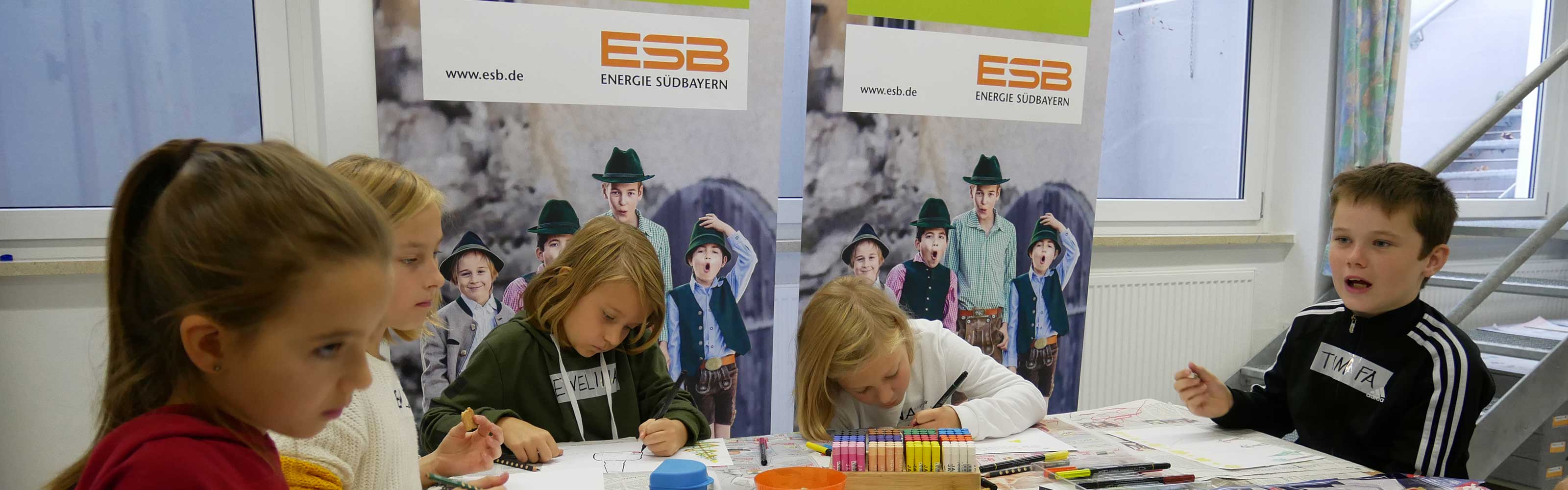 Fünf Kinder sitzen an einem Tisch und malen Weihnachtskarten, im Hintergrund sind Rollups der ESB