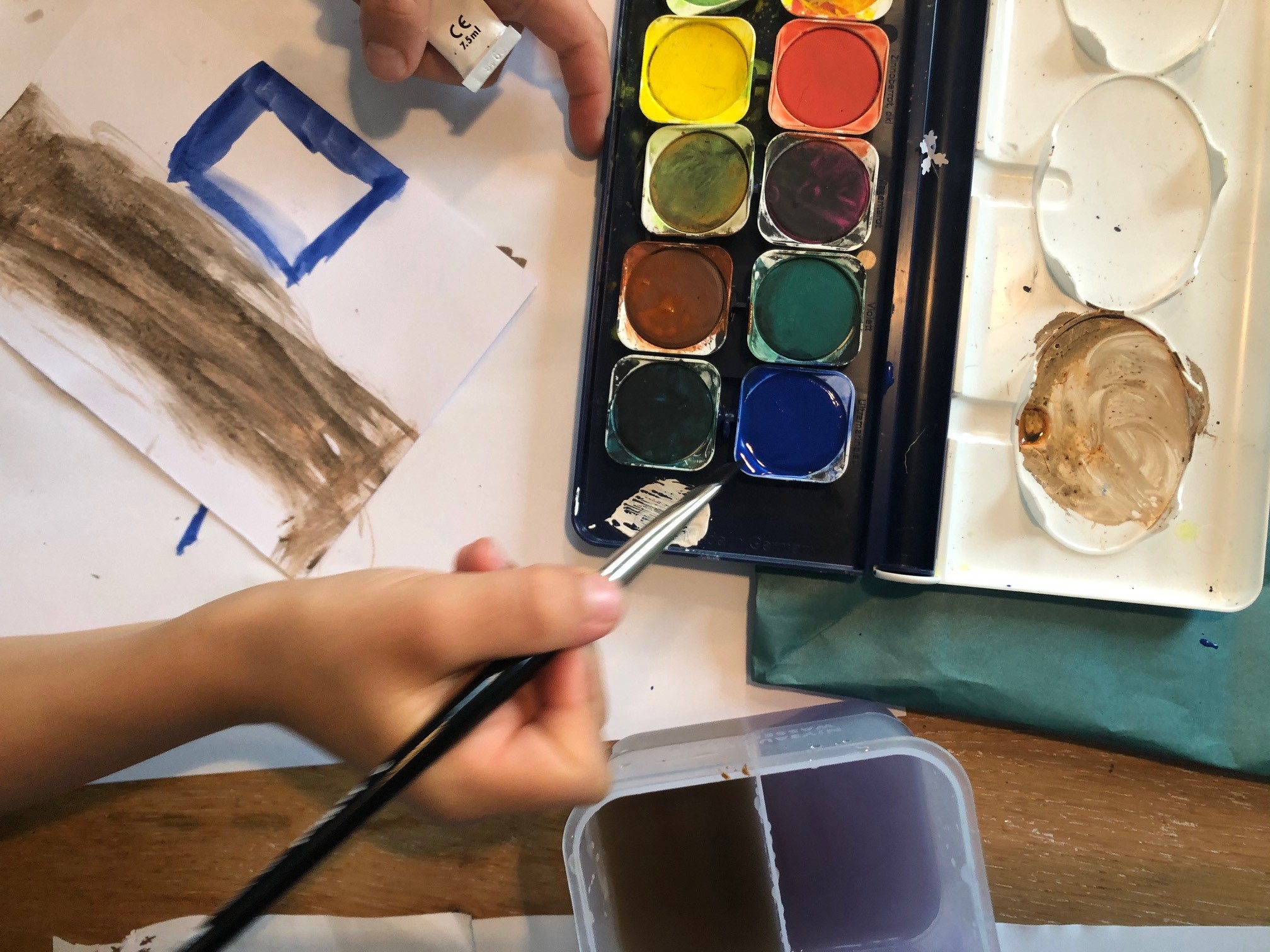 Ein Kind malt mit Wasserfarben eine Weihnachtskarte.